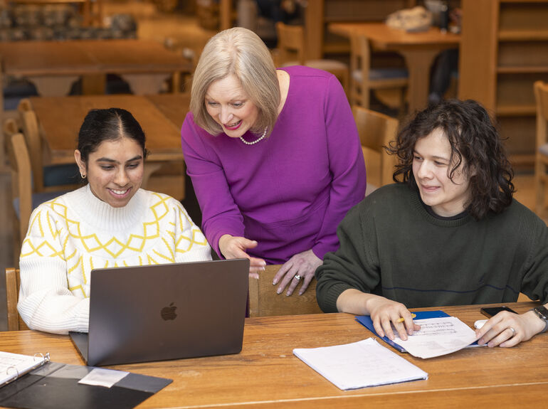 Dean Amy Smith in library standing behind 2 students at long table