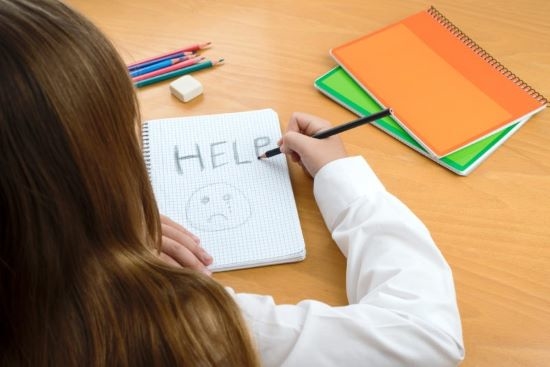Young female student in classroom who has written HELP in her notebook