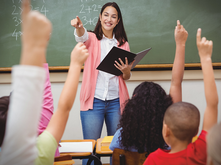 Teacher at front of class with students' raised hands